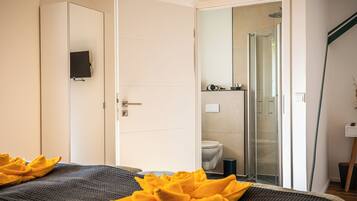 Quarto de hotel moderno com uma cama, área de chuveiro e vaso sanitário visíveis através de uma porta de vidro.