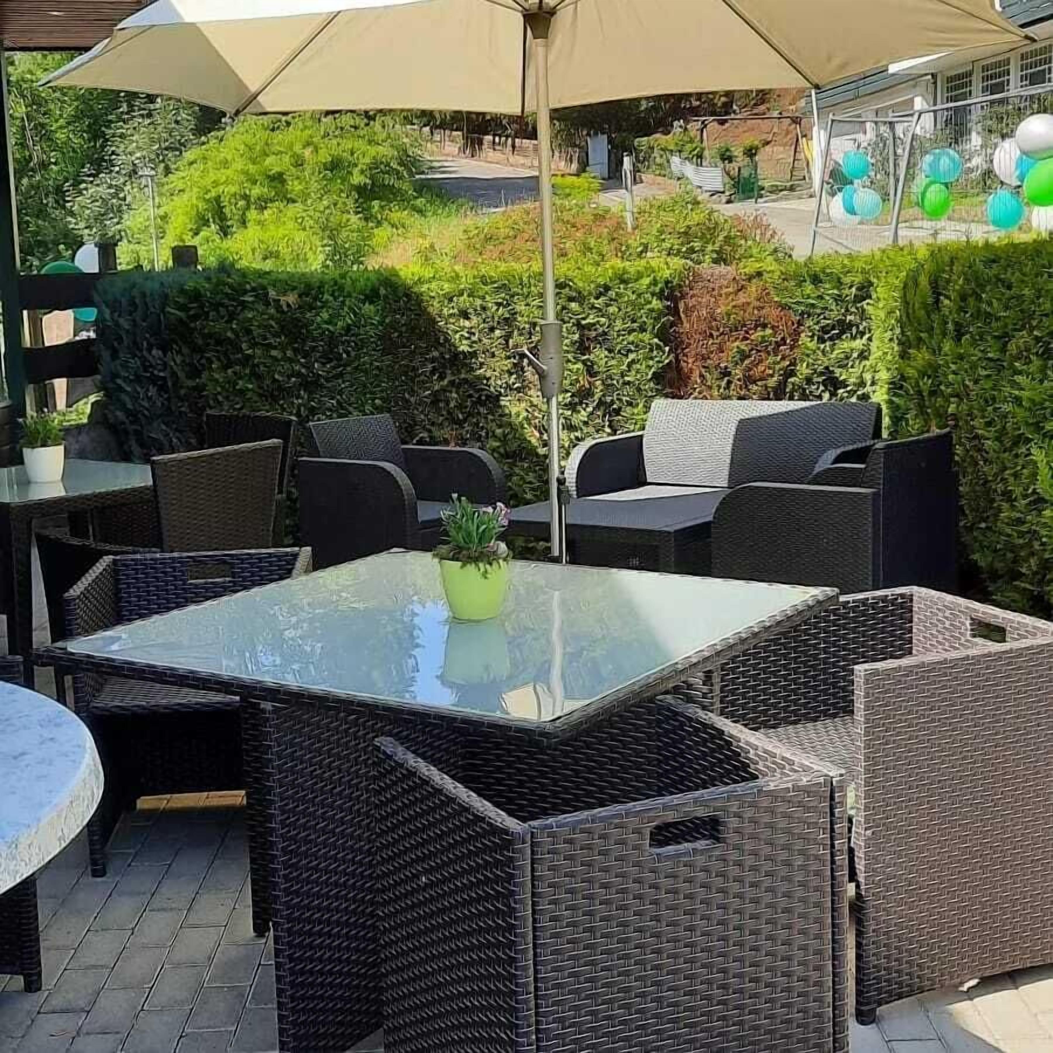 An outdoor patio with wicker furniture, a glass table, and a potted plant.