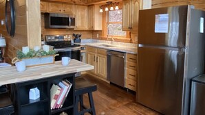 A modern kitchen with wooden cabinets, stainless steel appliances, and a wooden island with books and a decorative bowl. - Sugar Maple Sunset in Shagbark (Sevierville)