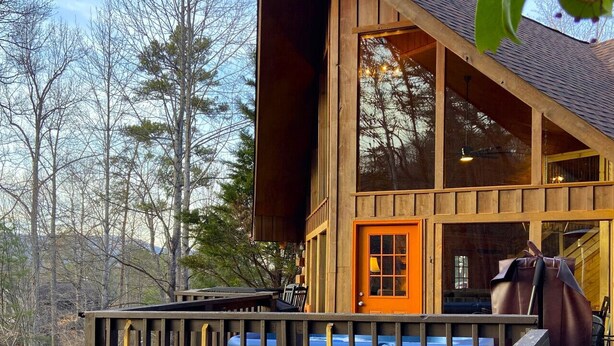 A wooden cabin with a prominent orange door, large windows, and a deck. - Sugar Maple Sunset in Shagbark (Sevierville)