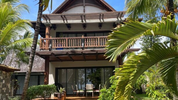 Un bâtiment à deux étages doté d’un balcon, entouré de palmiers et d’une pelouse bien entretenue.
