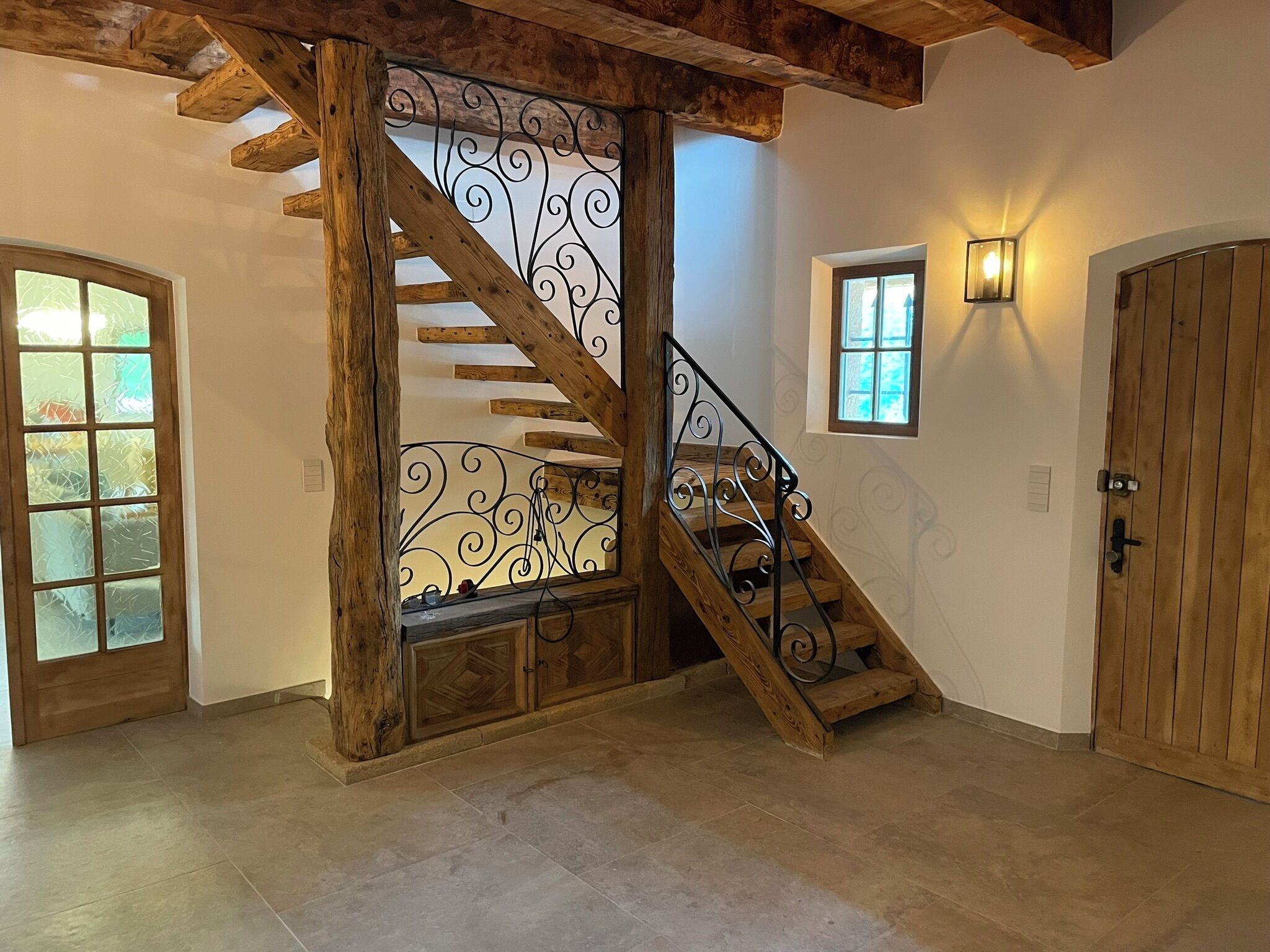 A wooden staircase with a wrought iron railing, a wooden door, and a small window with a light fixture.