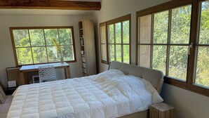 A bedroom with a bed, a desk, and large windows.