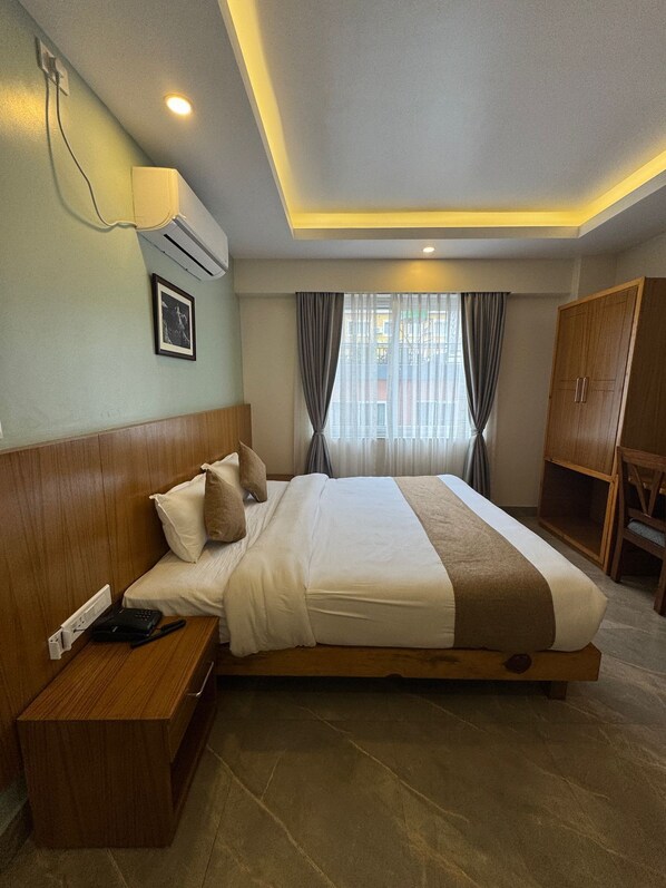 A hotel room with a large bed, wooden headboard, bedside tables, a wardrobe, and a window with curtains.