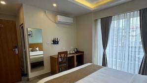 A hotel room with a large bed, a desk, a chair, a small table with a kettle, and a window with curtains. - Bay Hotel (Pokhara)