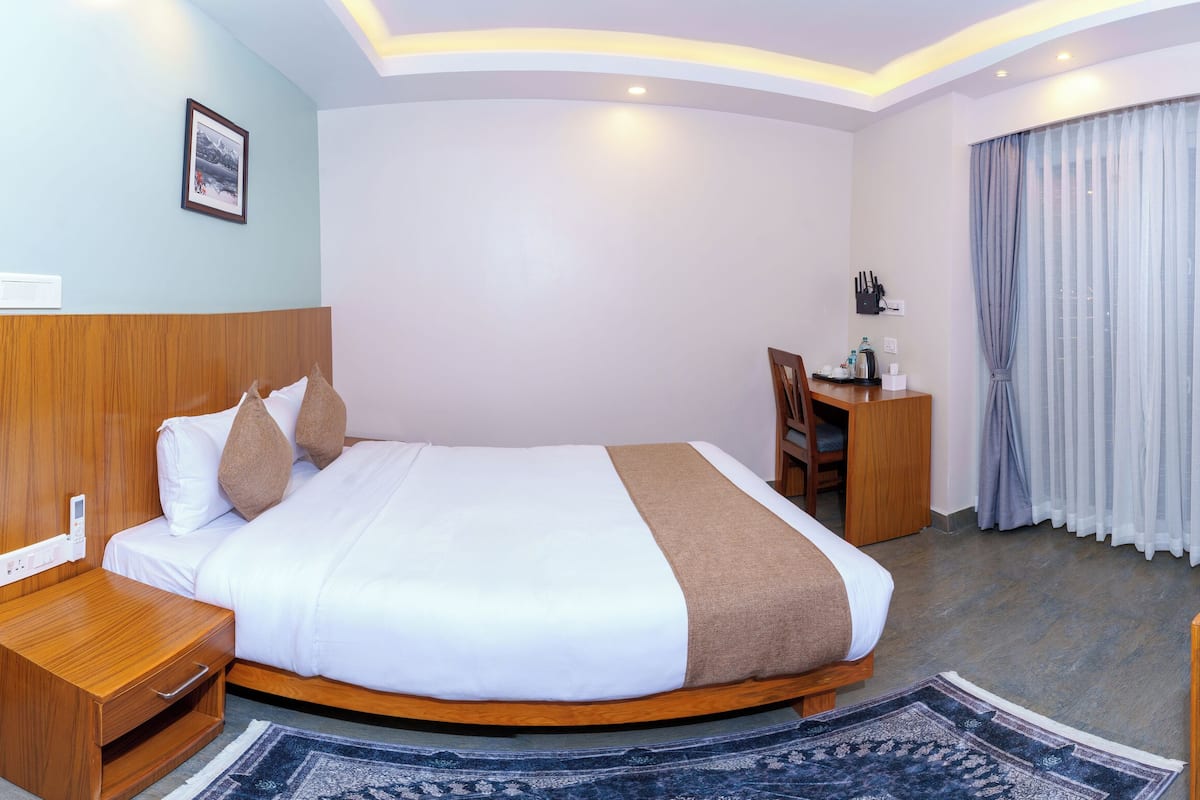 A hotel room with a wooden bed, a nightstand, a desk, and a chair.