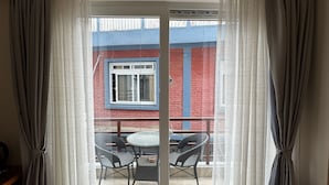 A room with a sliding glass door leading to an outdoor area with a table and chairs. - Bay Hotel (Pokhara)