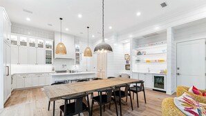 Una cocina moderna con armarios blancos, una mesa de comedor de madera, sillas negras y lámparas colgantes de mimbre.