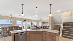 A spacious kitchen with a large island, wooden cabinets, and pendant lighting. There is a view of the ocean through large windows. - Gulf Front Home with Pool | Hot Tub (Port St Joe)