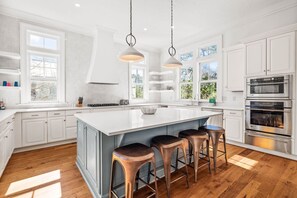 Une cuisine moderne avec des meubles blancs, un grand îlot central doté de tabourets et des appareils électroménagers en acier inoxydable.