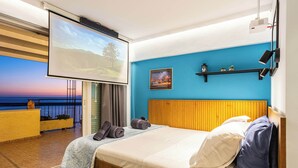 A bedroom with a bed, a TV screen, a balcony with a view, and a blue wall. - Beachfront Sunny Penthouse - Kalamata SeaBliss (Kalamata)