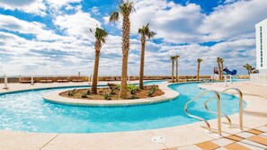 Un área de piscina con palmeras, sillas de descanso y un tobogán de agua.