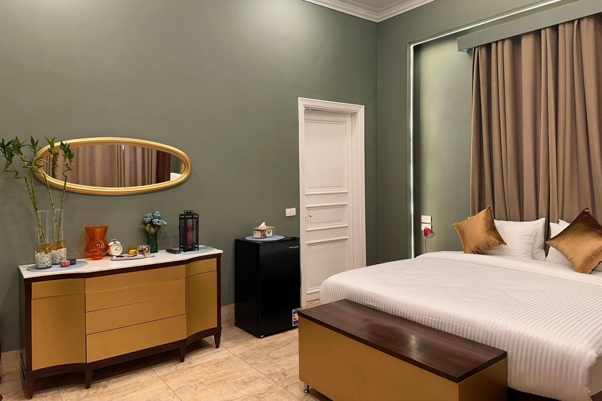 A bedroom with a bed, bedside table, dresser, mirror, and a door.