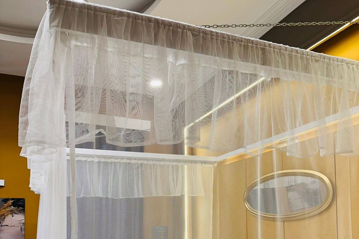 A hotel room with a bed, white bedding, a canopy, and a round mirror on the wall.