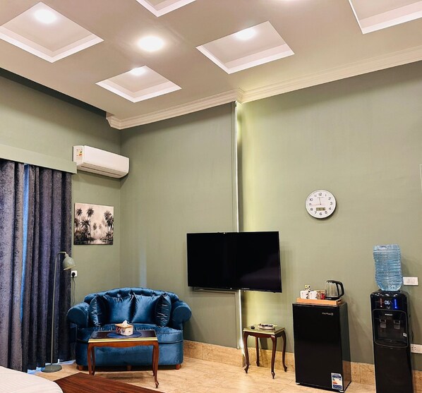 A living room with a blue sofa, a flat-screen TV, a water dispenser, and a clock on the wall. - GA PLUS (Cairo)