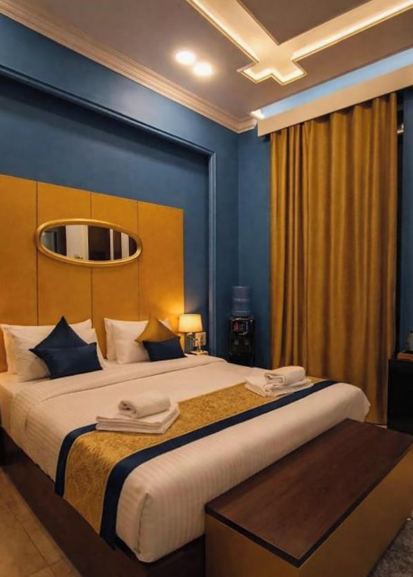A hotel room with a large bed, a bedside table, a mirror, and a window with curtains. - GA PLUS (Cairo)