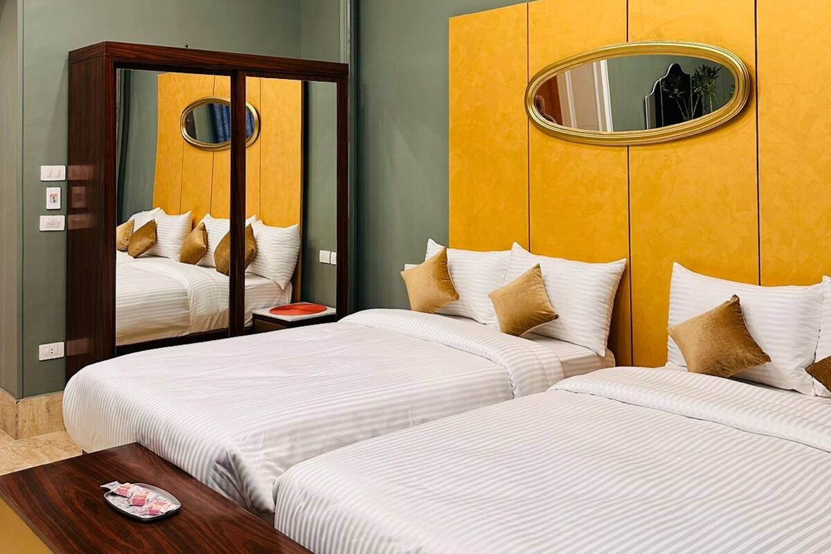 A hotel room with two beds, a wooden wardrobe, a mirror, and a small table with a tray.
