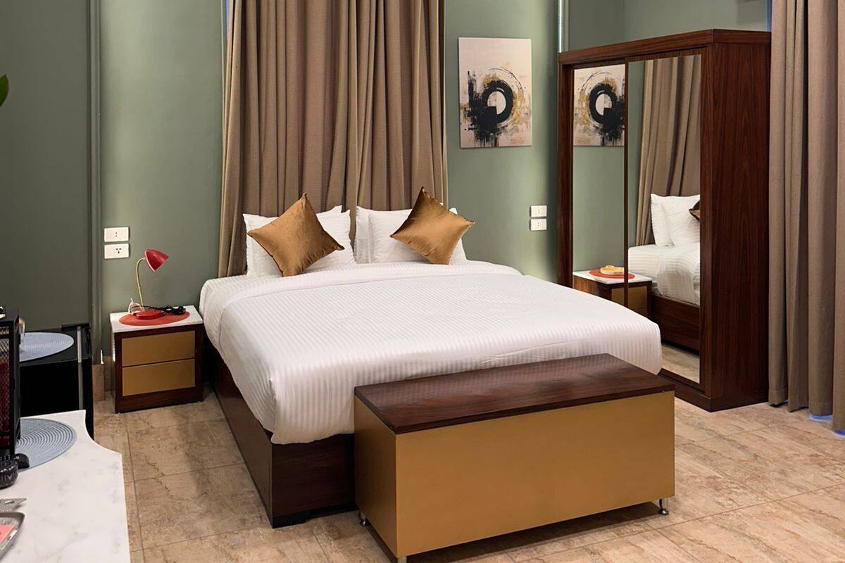 A modern hotel room with a large bed, a bedside table, a mirror, and a wooden bench.