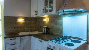 Une cuisine compacte avec des meubles blancs, une cuisinière à gaz, une bouilloire et un four encastré.