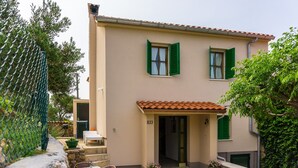 Un bâtiment à deux étages, doté d’une façade beige, de volets verts et d’un toit en tuiles. On y trouve un petit espace extérieur aménagé avec une table et des chaises.