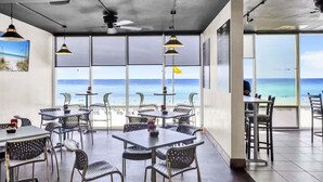 Un restaurante con mesas y sillas, ventanas amplias y vista a la playa.