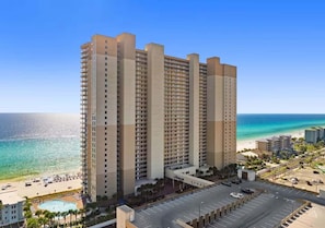 A high-rise hotel with a pool, beach view, and parking lot.