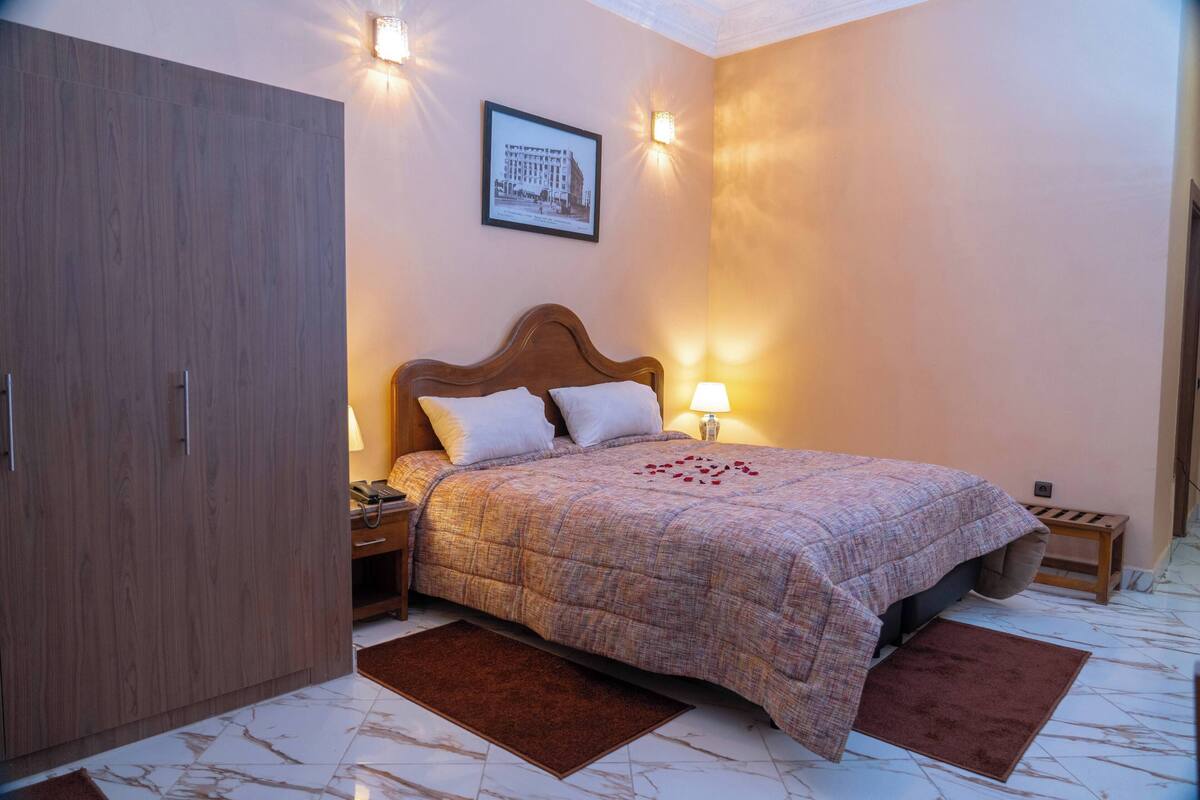 Een slaapkamer met een houten garderobe, een bed met een decoratief sprei, twee bedlampen en een ingelijst schilderij aan de muur.