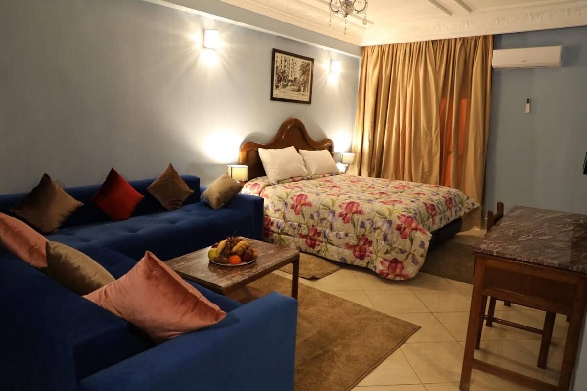Een gezellige woonkamer met een blauwe bank, een bloemenbedekker en een klein tafeltje met fruit.