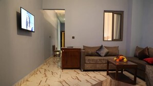 Una sala de estar con un sofá, una mesa de centro con fruta, un televisor montado en la pared y un piso de mármol.