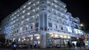 Un hotel de varios pisos con balcones, una entrada principal y banderas.