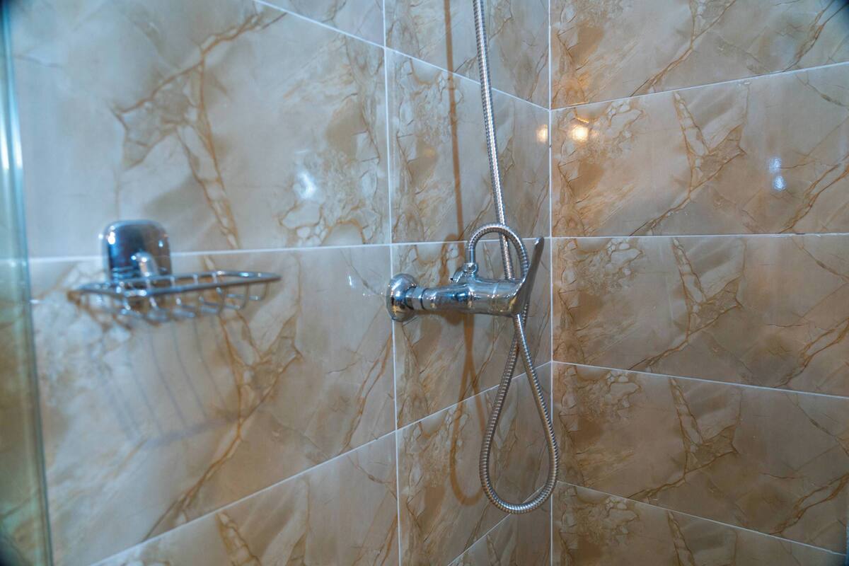 Een badkamer met marmeren tegels en een douche met handdouche.