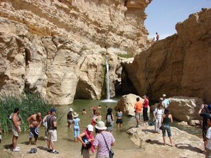 A natural rock formation with a waterfall, surrounded by people enjoying the area. - Villa Atlas Osis (As-Sabikah)