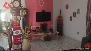 A living room with a large clock, a television, and a guitar. - Villa Atlas Osis (As-Sabikah)