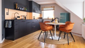A modern kitchen with dark cabinetry, a white dining table, and orange chairs.
