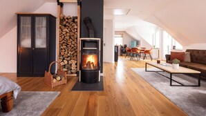 A modern living room with a wood-burning stove, a dining area with a table and chairs, and a cozy seating area with a sofa and cushions.