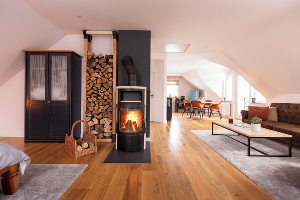 Una sala moderna con una estufa de leña, un comedor con mesa y sillas, y una zona de estar acogedora con sofá y cojines.