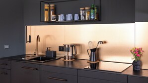 A modern kitchen with a black countertop, stainless steel appliances, a coffee maker, and a shelf with jars and cups.