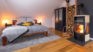 A bedroom with a bed, bedside lamps, a fireplace, and a stack of firewood.