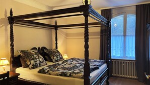 Una cama con dosel, ropa de cama floral, una mesita de noche y una lámpara.