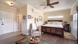 Ein Schlafzimmer mit einem großen Bett, einem Deckenventilator, einem Holzkopfteil, einem Nachttisch mit Lampe und einem Fenster mit Jalousien.