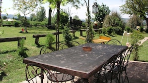 Une terrasse extérieure avec une table et des chaises, entourée de verdure et d’une clôture rustique.