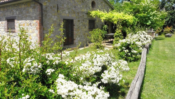Un bâtiment en pierre avec un jardin, une clôture en bois et un banc.