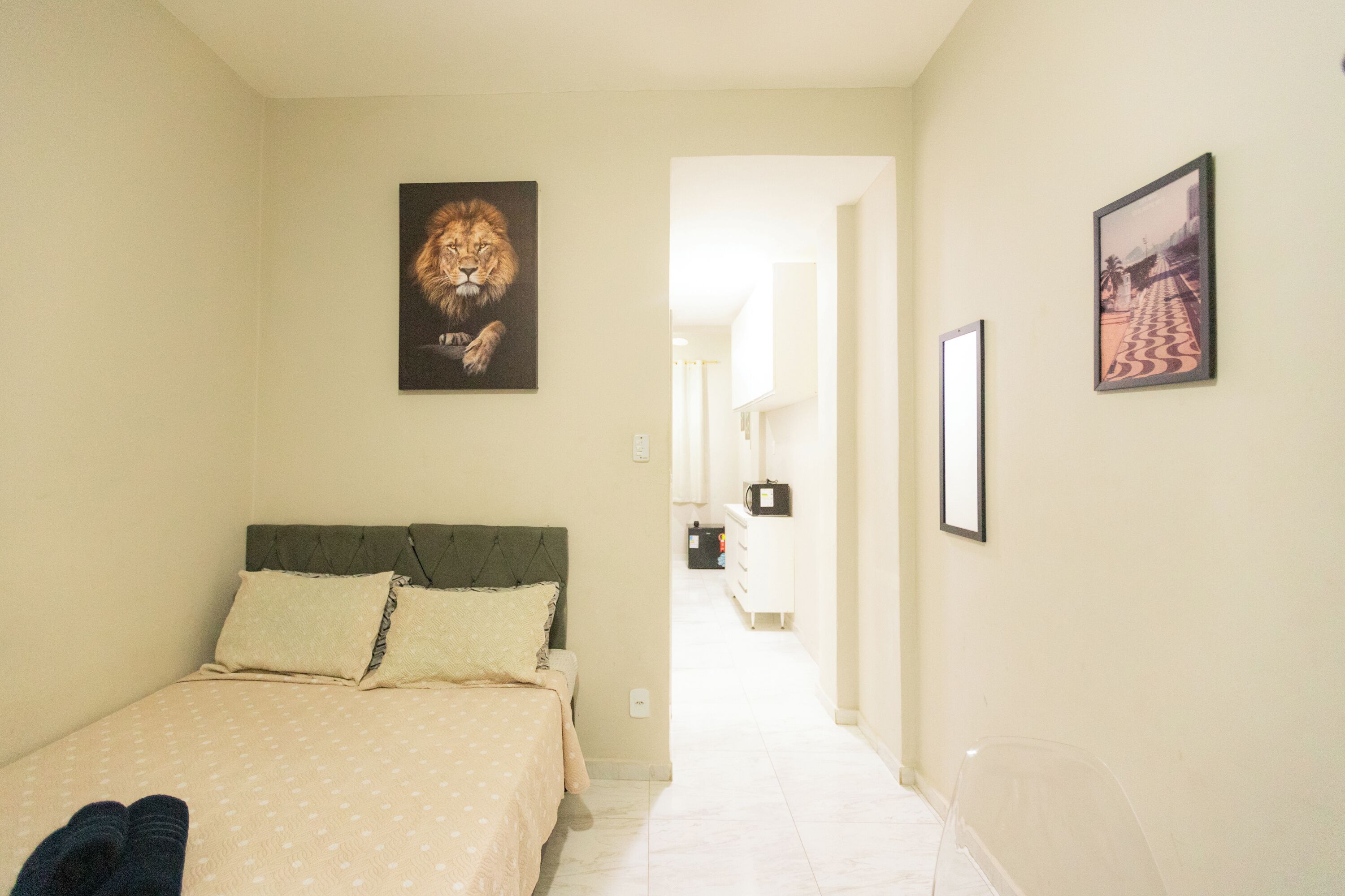 A bedroom with a bed, pillows, a lion painting, and a corridor leading to a bathroom.