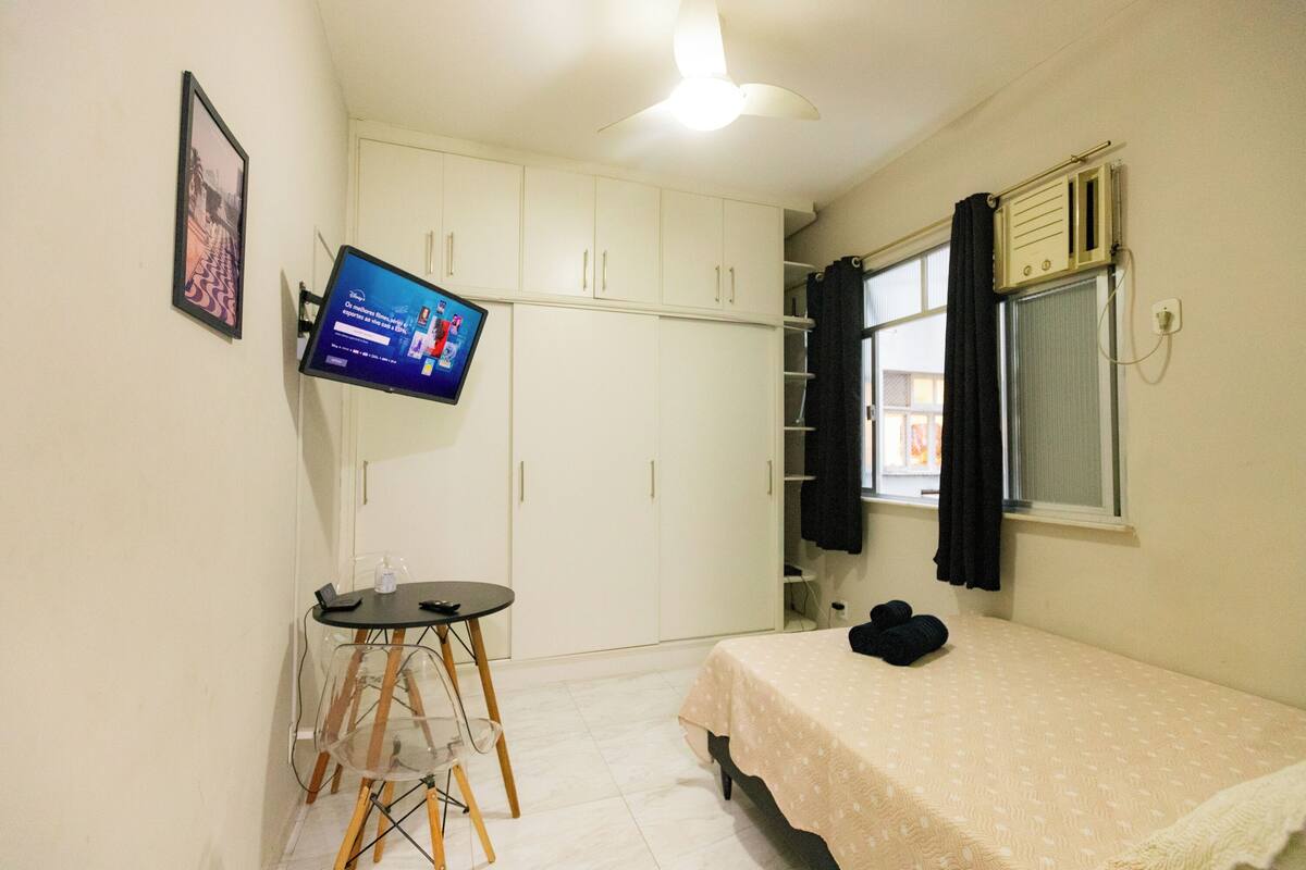 A bedroom with a bed, a desk with a chair, a TV, and a wardrobe.