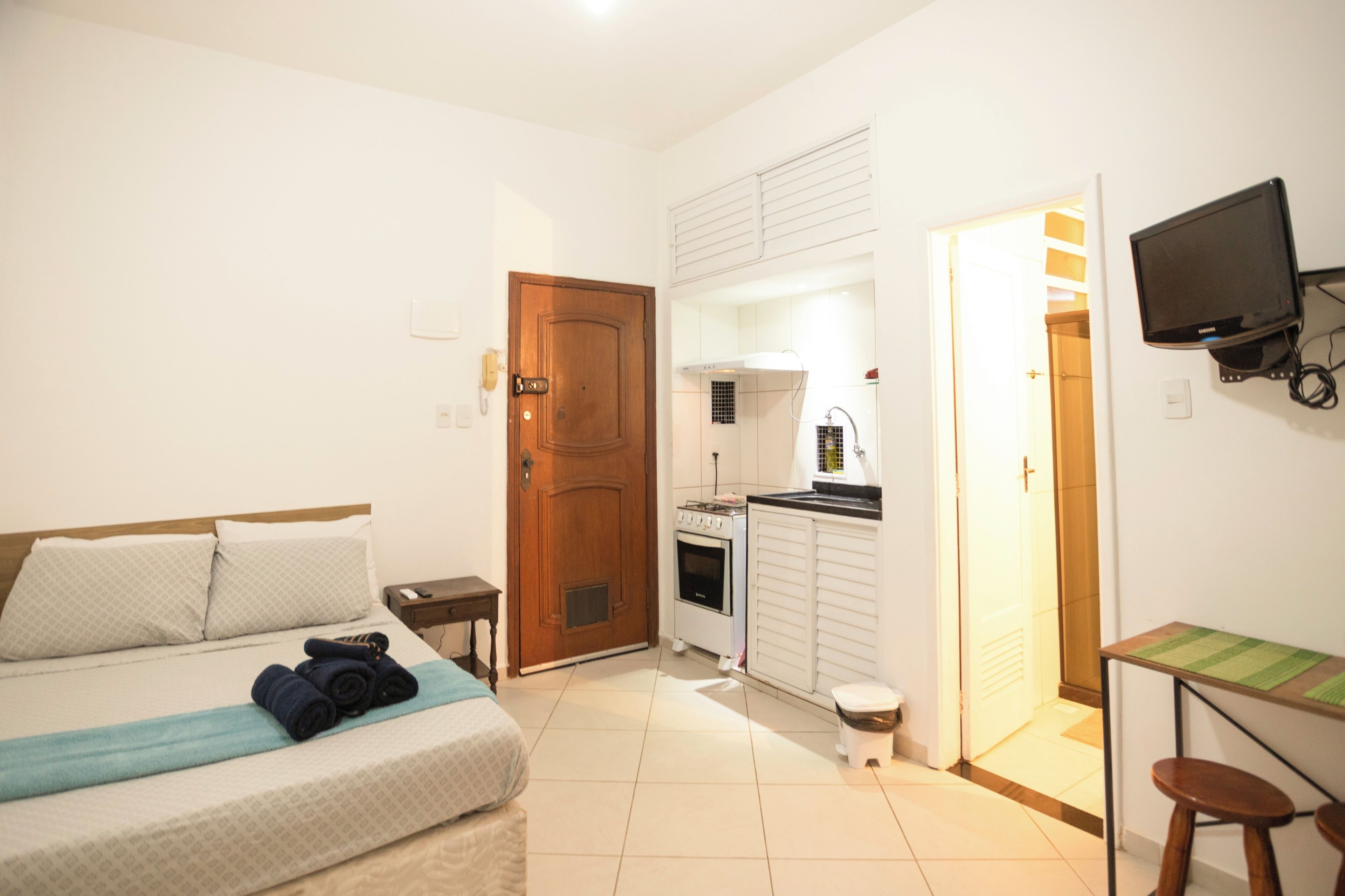 A compact hotel room with a bed, a small kitchenette, a TV, and a bathroom.