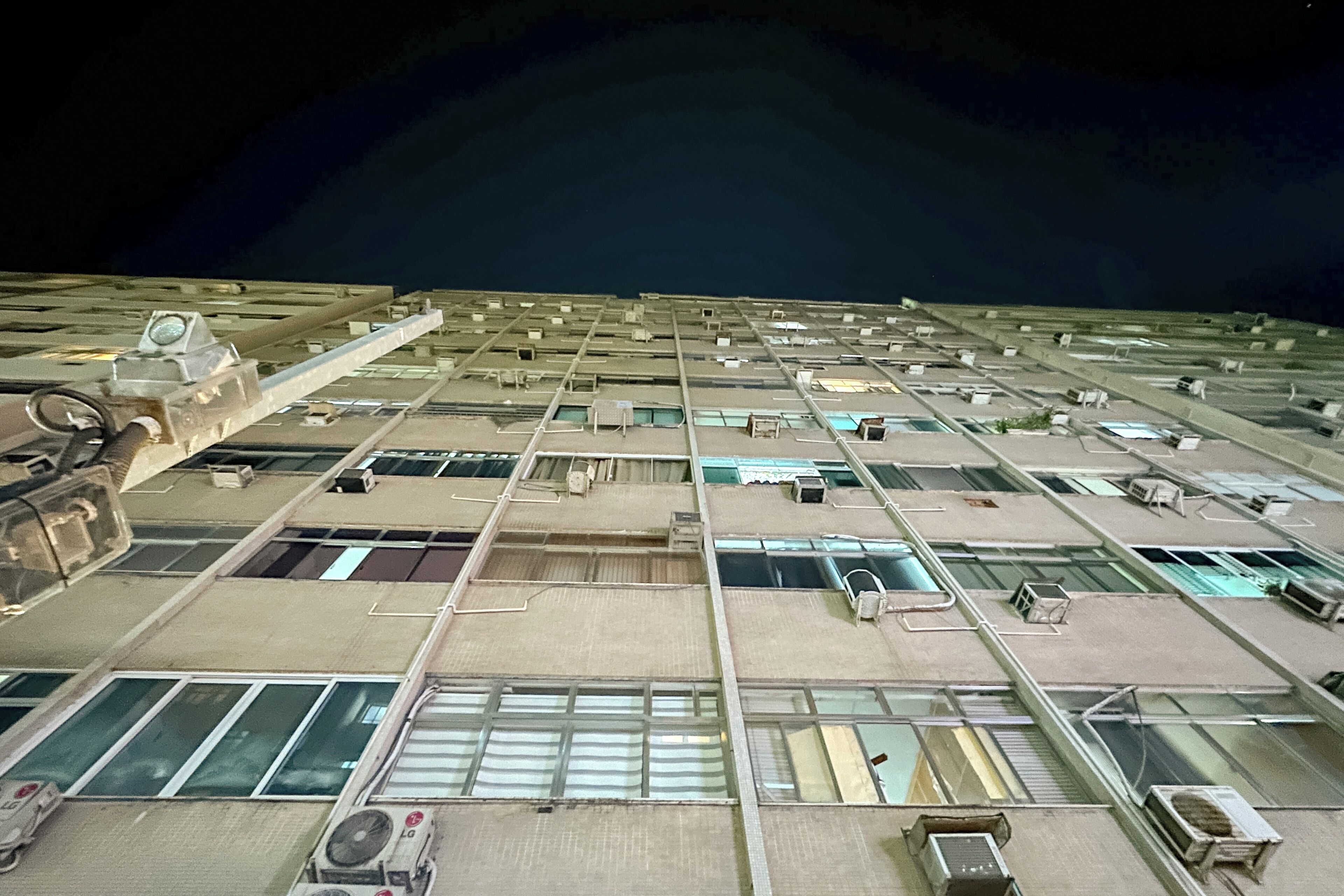A large building with multiple floors, each with numerous windows and air conditioning units.