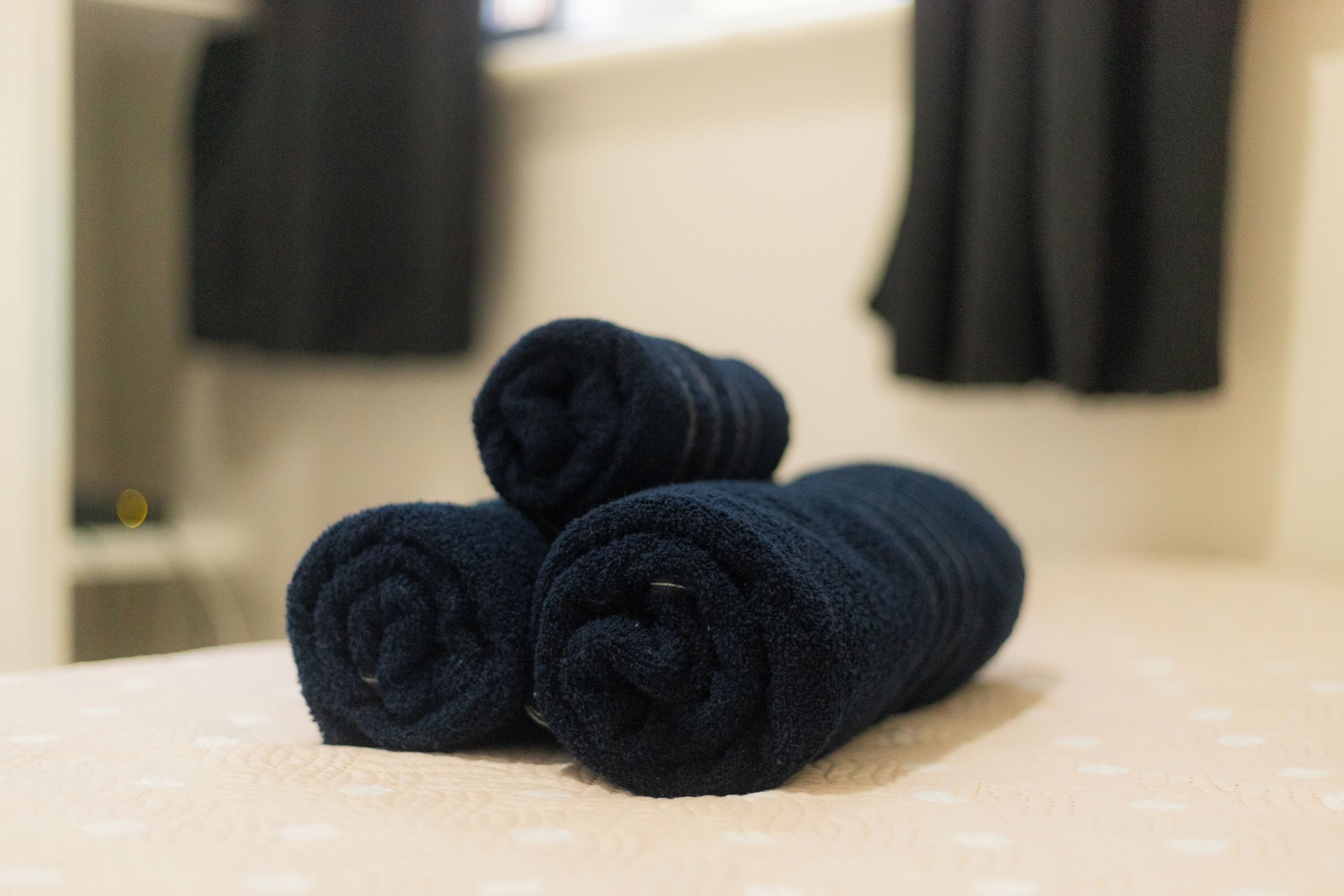 Una toalla azul marino doblada cuidadosamente sobre una cama con una colcha estampada.