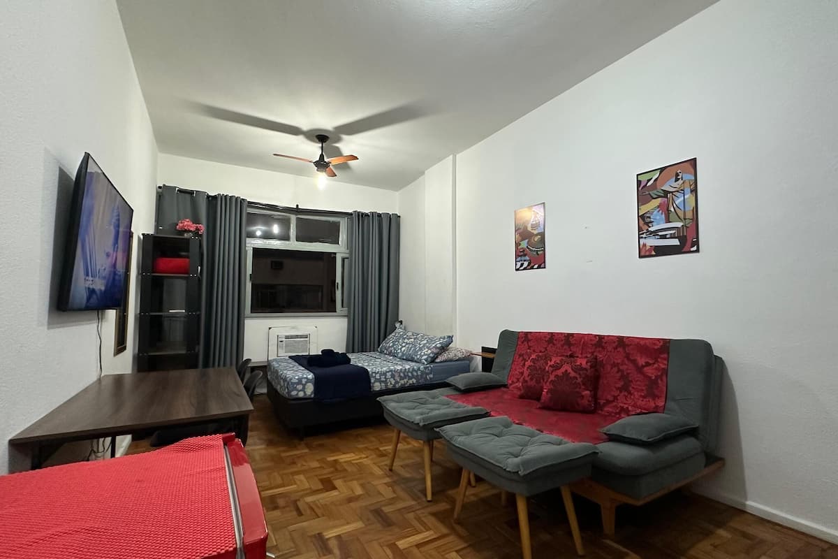 A compact room with a bed, a sofa, a small table, and a ceiling fan.