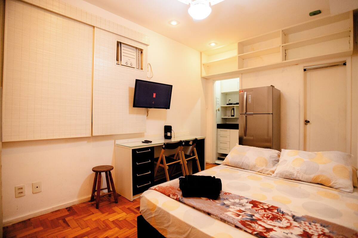 A bedroom with a bed, a desk, a chair, a television, a refrigerator, and a microwave.
