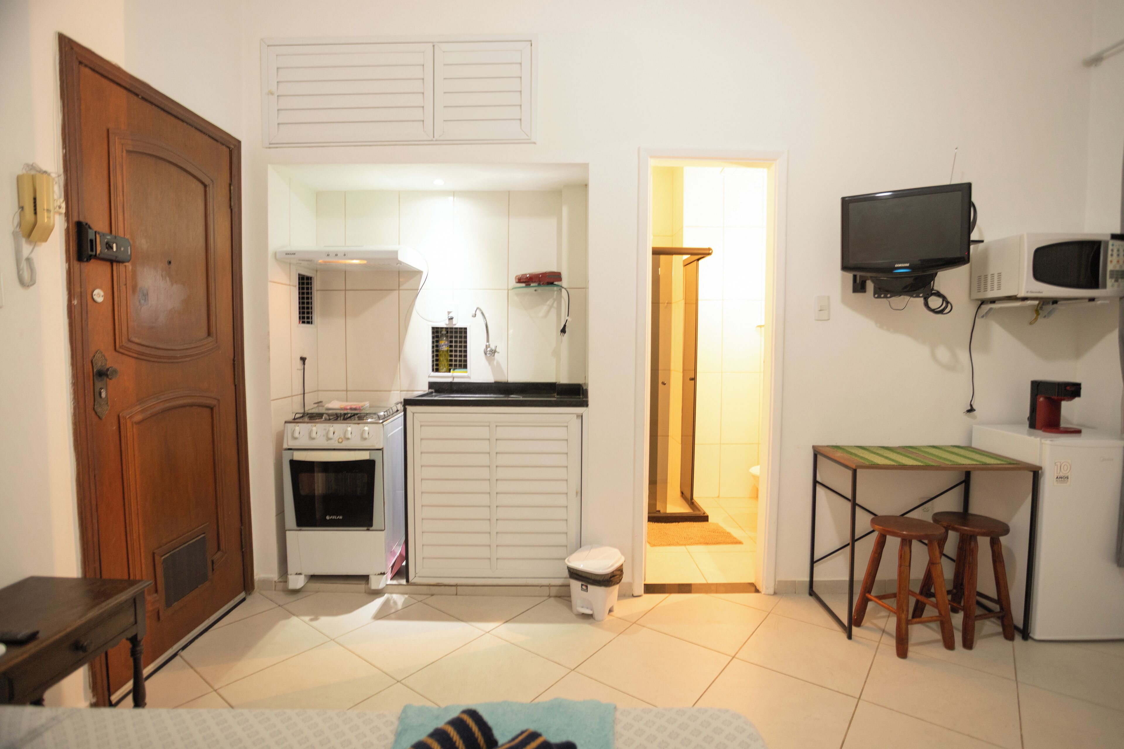 A compact kitchen with a stove, microwave, and a small table with stools.